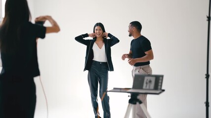 Professional female photographer guiding two diverse models during collaborative photoshoot, creating dynamic visual content with precise studio lighting and professional posing