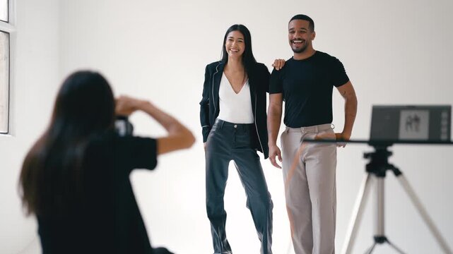 Photographer taking photos of two fashion models posing together in a professional studio setting with white background