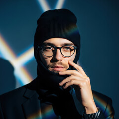 Stylish young man in a black beanie and turtleneck poses under artistic light with a thoughtful expression
