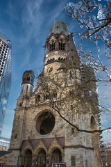 Kaiser Wilhelm Memorial Church, Berlin - The ruined tower of the iconic Ged&auml;chtniskirche, a poignant WWII memorial contrasting with modern architecture under a blue sky.