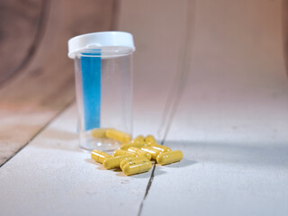 Spilled Yellow Capsules, Pill Bottle - Close-up of yellow capsule pills spilled from an empty prescription bottle on a textured white surface, symbolizing health, dosage, and medical care.