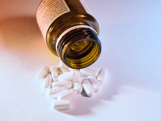 White Pills Spilled from Medicine Bottle - White oval pills spilled from an open brown prescription bottle on a clean white background. Concept for health, medication, pharmacy, and dosage.