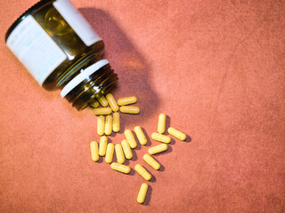 Yellow Capsules Spilling from Bottle - Vibrant yellow capsules spilling from an amber glass bottle onto a textured reddish-brown surface. Ideal for health, medicine, and wellness concepts.