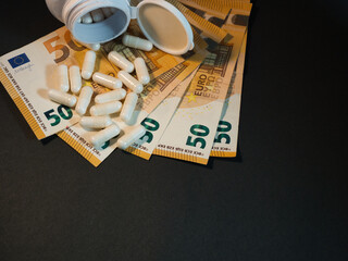 Healthcare Costs: Euro Banknotes & Pills - White capsules spill from an open bottle onto fanned 50 Euro banknotes, illustrating the escalating costs of medication and healthcare expenses.