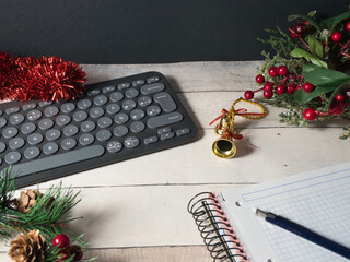 Festive Workspace with Keyboard - A contemporary dark keyboard surrounded by festive red tinsel, golden bells, and green pine branches on a rustic wooden desk, perfect for holiday season work.
