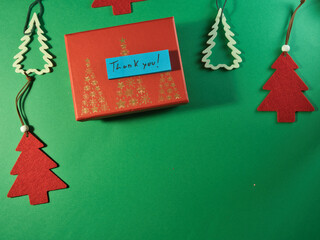Christmas Thank You Gift and Ornaments - Festive red gift box with handwritten 'Thank You!' message and various Christmas tree decorations on a cheerful green surface. Ideal for holiday appreciation.