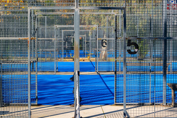 View of a padel court with open doors and bright blue playing surface in the afternoon sun