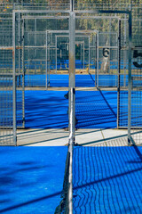 View of a padel court with open doors and bright blue playing surface in the afternoon sun