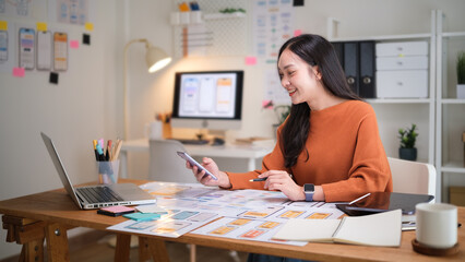 UX UI designer reviewing mobile app layouts while holding a smartphone and comparing interface elements on paper prototypes.