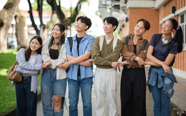 Group of university students standing together outdoors, smiling and linking arms in a friendly, supportive pose on campus.