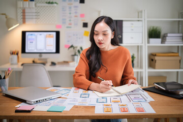 Professional UX UI designer planning user interface concepts, analyzing wireframe prototypes at a modern desk.