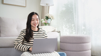 Smiling woman using a laptop while sitting comfortably at home. Remote work, online communication, and modern lifestyle concept.