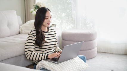 Young woman sitting on the floor at home using a laptop, working in a cozy living room. Remote work and digital lifestyle concept.