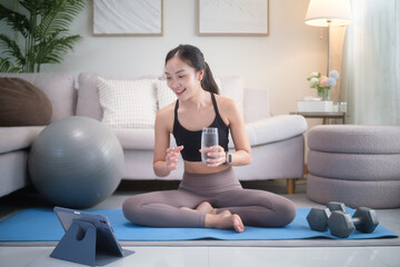 Woman exercising at home on a yoga mat, following an online workout on a tablet. Home fitness, digital training, and healthy lifestyle concept.