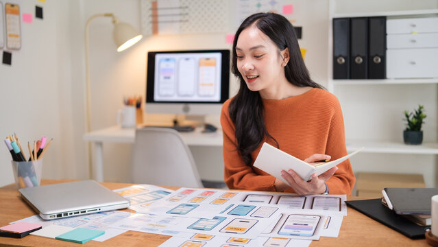Professional UX UI designer working at a home office, reviewing mobile app wireframes and user interface layouts on printed sheets.