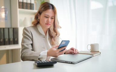 Businesswoman checking her smartphone while working at a modern office desk.