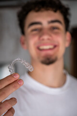 Smiling young man holding a transparent orthodontic retainer, representing modern dental care and teeth straightening for a perfect smile