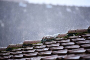 Rainwater streams down the edge of a sloped roof against a misty mountain backdrop, creating a dramatic, atmospheric scene.