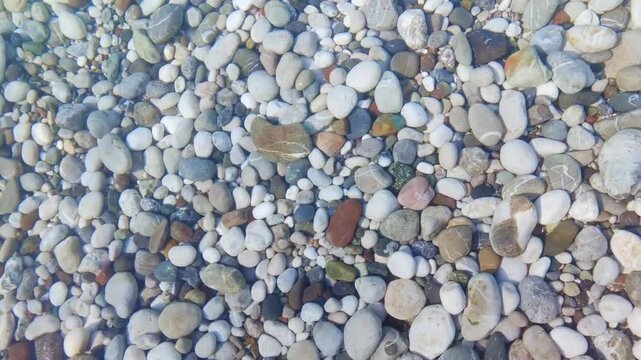 Beautiful close up hd video view of sea waves washing over colorful rounded pebbles on beach white foam tranquil sea landscape texture footage from above perfect for campaigns