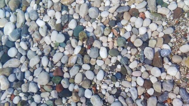 Beautiful close up hd video view of sea waves washing over colorful rounded pebbles on beach white foam tranquil sea landscape texture footage from above perfect for campaigns