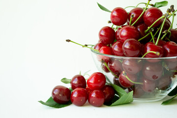 Ripe cherries in glass bowl with leaves on white background