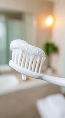 Toothbrush with foamy toothpaste held in hand, set against a blurred bathroom background, emphasizing the importance of oral hygiene and daily tooth cleaning routine