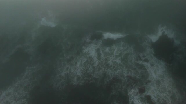 Aerial drone view of foggy Portugal coast with camera moving down toward ocean waves