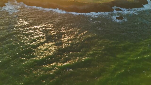 Aerial drone view over ocean with camera moving up above shimmering water, northern Spain