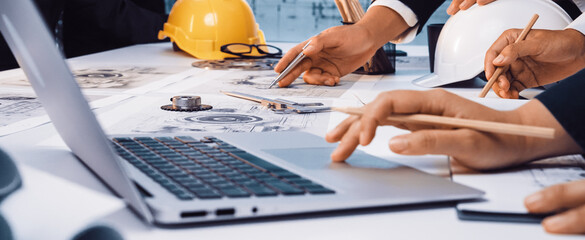 A diverse engineering team collaborates on technical plans using a laptop and construction tools. The workspace reflects a modern and creative environment for innovative projects. SACTR