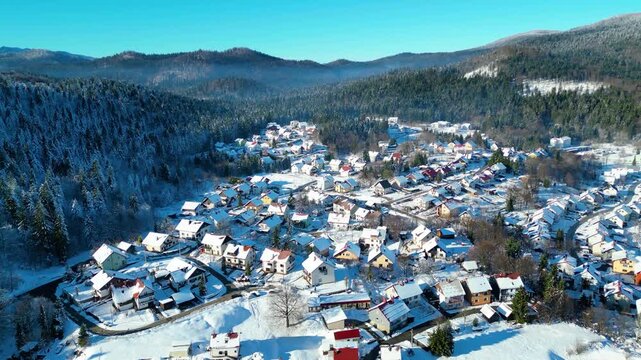 Aerial view of snow-covered Delnice, Croatia, nestled in a valley with a distant cloud inversion. Winter landscape under a clear blue sky. Perfect for winter travel.