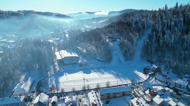 Aerial view of a snow-covered Delnice nestled in a mountain valley under a clear winter sky, showcasing pristine natural beauty and urban life.
