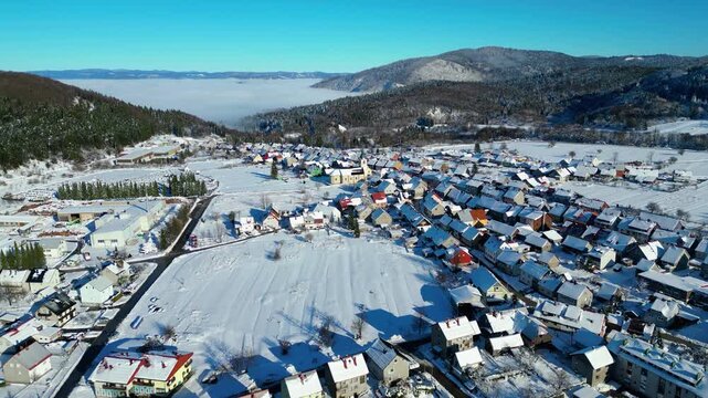 Aerial view of snow-covered Delnice, Croatia, nestled in a valley with a distant cloud inversion. Winter landscape under a clear blue sky. Perfect for winter travel.