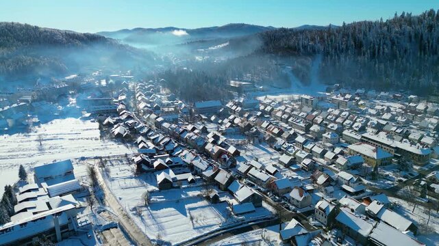 Aerial view of Delnice, Croatia, blanketed in pristine winter snow. Sunlit roofs and frosted forests create a picturesque scene in Gorski Kotar.