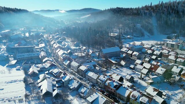 Aerial view of Delnice, Croatia, blanketed in pristine winter snow. Sunlit roofs and frosted forests create a picturesque scene in Gorski Kotar.