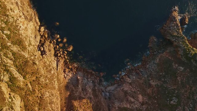 Birds-eye aerial drone view of coastal cliff mountain and blue ocean bay with bird flying, drone moving right Spain