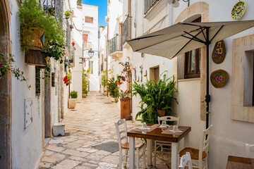 Cozy cafe tables along a narrow whitewashed alley decorated with plants and flowers in Locorotondo town, Apulia, Italy
