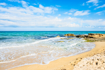 Golden sandy beach with turquoise waves gently rolling under a bright blue sky in Peschici town. Apulia, Italy