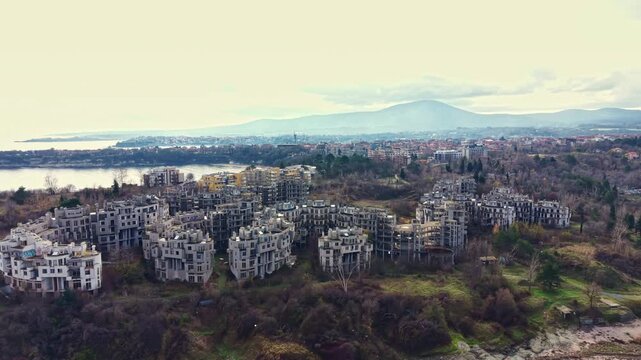 Crumbling structures of an abandoned development overlook a tranquil body of water, life halted in time amidst nature's gradual reclaiming of the landscape.