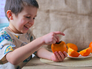 Happy Young Boy Enjoying a Healthy Snack of Fresh Ripe Persimmons - Smiling Child Playing with Vibrant Orange Persimmon Fruits at a Wooden Table