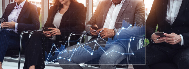 Business professionals interact with smartphones while reviewing financial charts in a contemporary office, showcasing collaboration and modern technology in a vibrant setting. Scalp