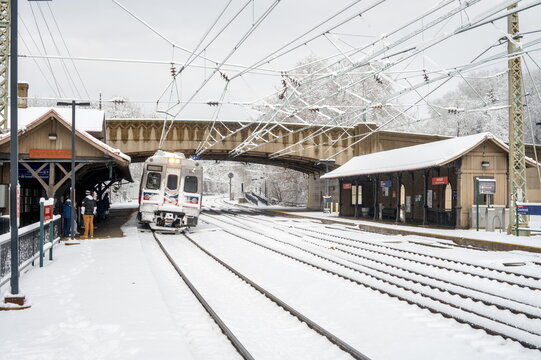 A SEPTA Regional Rail train pulls into the historic Overbrook Station during a heavy winter snowstorm. Commuters wait on the snow-covered platform of the Paoli/Thorndale Line in West Philadelphia.