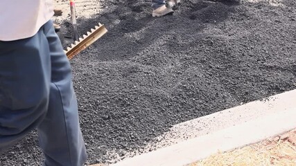 Workers are leveling new asphalt on parking lot with large brooms in commercial area.