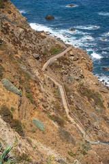 Steep wooden staircase descending rugged volcanic cliffs toward turquoise ocean waves and rocky shoreline near Benijo beach, Tenerife, Canary Islands, Spain.