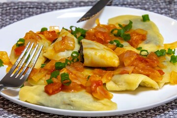 Traditional pierogi filled with black beans in a sauce of onions, fresh tomatoes, and fresh green onions. Traditional Ukrainian food.