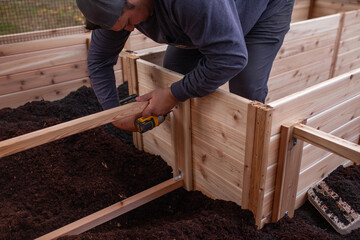 Assembling and filling a backyard kitchen raised garden bed with a mix of soil and compost. Cedar side supports help prevent bowing once the bed is filled with soil.