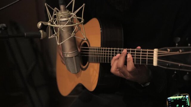 Man playing guitar in front of microphone in music studio