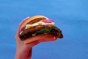 Isolated Beef Burger in Hand on Vibrant Blue Background