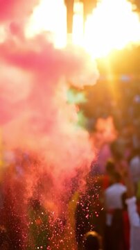 Backlit vertical video of the energetic holi festival crowd throwing vibrant pink powder into the warm golden sunlight.