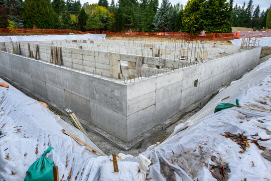 Large Stormwater Retention Tank project under construction, foundation dug and concrete poured, rebar and wood forms remaining, new housing development
