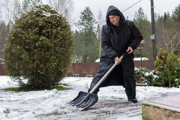 Senior male removing snow near house and garden highlighting cold weather routine and physical activity.